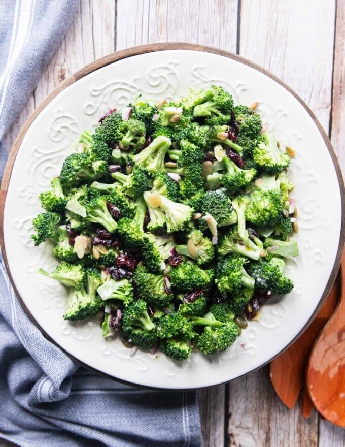 Creamy broccoli salad on a white plate with cranberries, sunflower seeds and onions 
