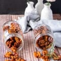 two jars of glossy candied walnuts in a jar spilling on a wooden board