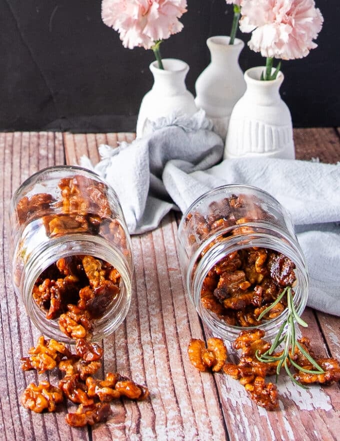 two jars of glossy candied walnuts in a jar spilling on a wooden board 