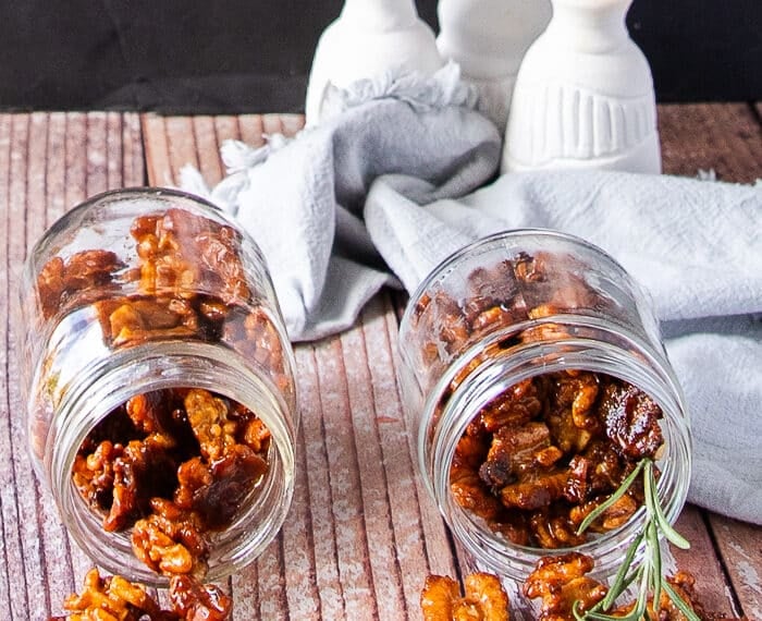 two jars of glossy candied walnuts in a jar spilling on a wooden board