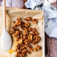Walnuts spread on parchment paper in a baking sheet to cool down