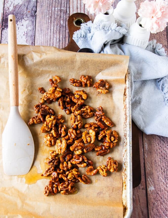 Walnuts spread on parchment paper in a baking sheet to cool down 