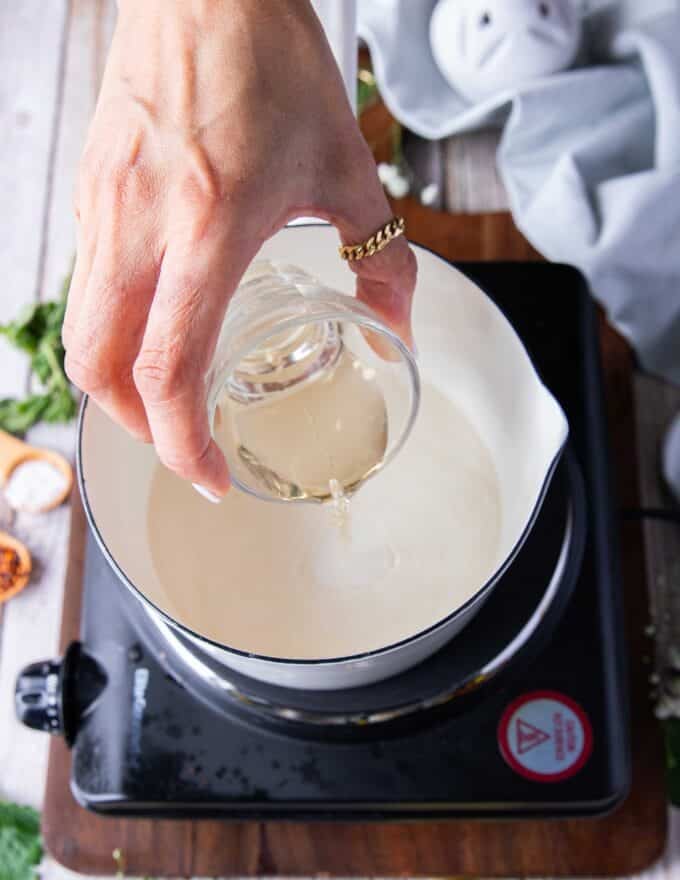 making the beurre blanc, a hand pouring in the white wine in a pot 