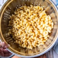 A HAND HOLDING cooked pasta in a drainer