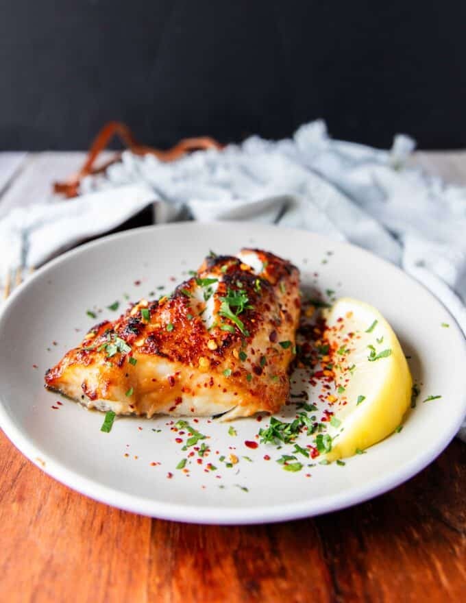 Miso glazed chilean sea bass with some lemon wedges on a plate 