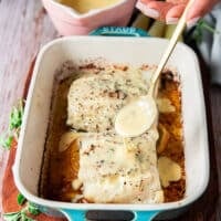 a hand drizzling some citrus beurre blanc over the baked chilean sea bass