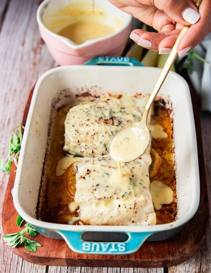 a hand drizzling some citrus beurre blanc over the baked chilean sea bass 