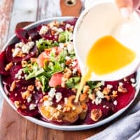 The dressing is being poured generously over the beet carpaccio dish