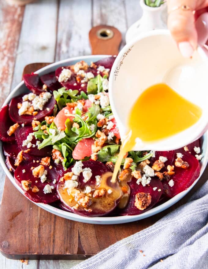 The dressing is being poured generously over the beet carpaccio dish