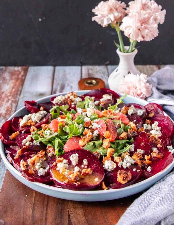 Close up of a beautiful beet carpaccio plate with sliced beets, arugula, walnuts, citrus segments and cheese