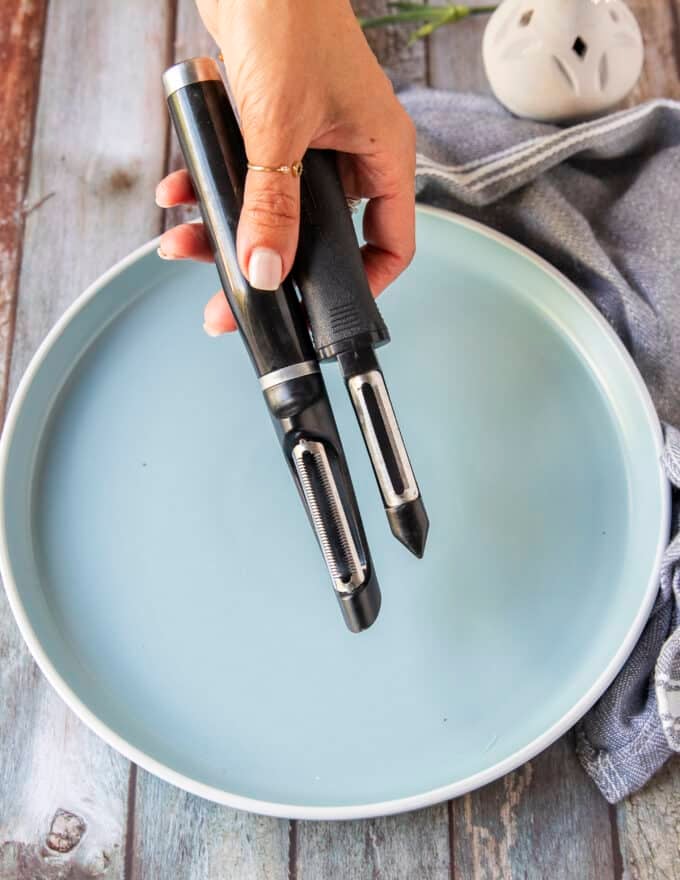 A hand holding a vegetable peeler and mandolin to start slicing the beets