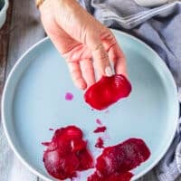 A hand holding paper thin slices of beets using a mandolin or vegetable peeler