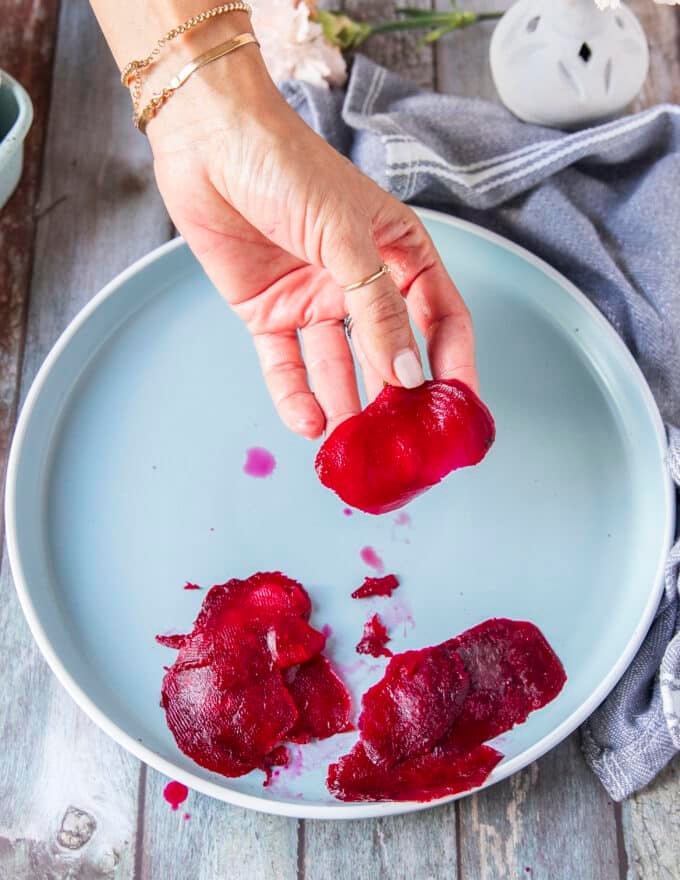 A hand holding paper thin slices of beets using a mandolin or vegetable peeler