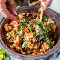 A hand scooping some cauliflower salad with almonds, raisins and chickpeas in tahini dressing using two spoons close up showing the textures