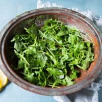 arugula is added to a large bowl to start assembling the cauliflower salad