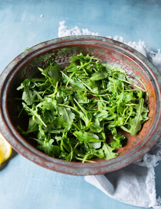 arugula is added to a large bowl to start assembling the cauliflower salad 