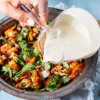 Tahini sauce is generously being poured over the cauliflower salad