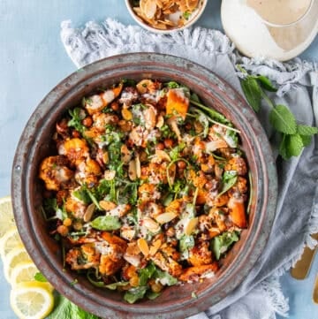 A large bowl of cauliflower salad with chickpeas, raisins, nuts, carrots and a tahini dressing