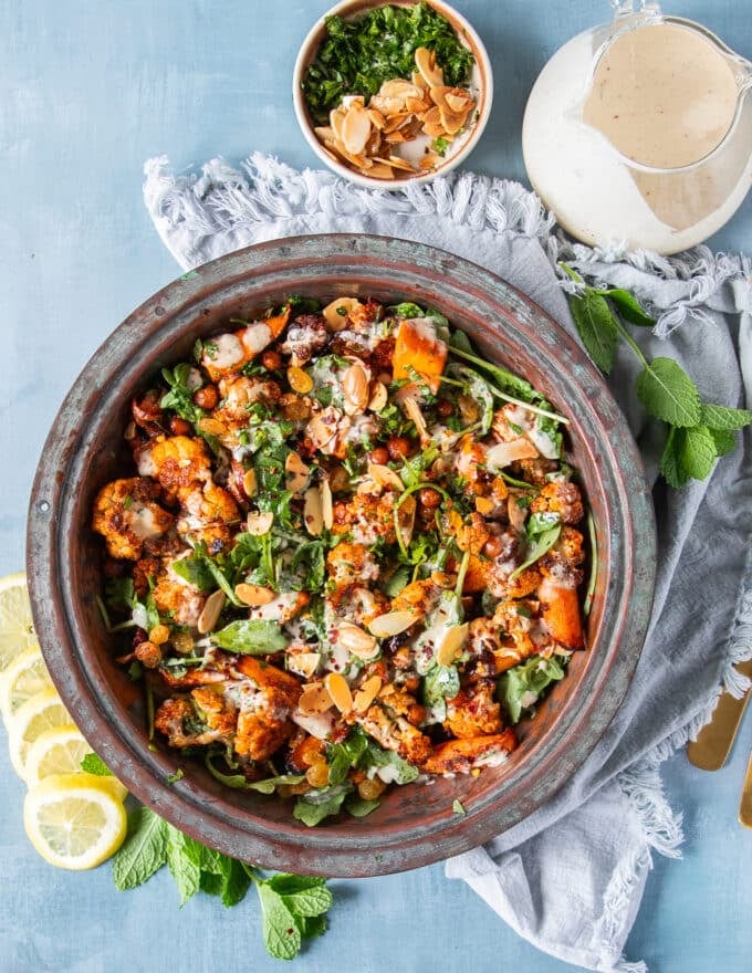 A large bowl of cauliflower salad with chickpeas, raisins, nuts, carrots and a tahini dressing 