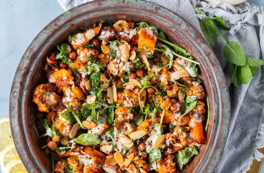 A large bowl of cauliflower salad with chickpeas, raisins, nuts, carrots and a tahini dressing