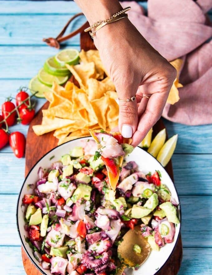 A hand holding a chip scooping octopus ceviche with lime, chillies and onion 