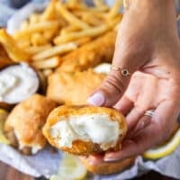 A hand holding a bitten fish showing close up the crispy crust and the succulent fish inside
