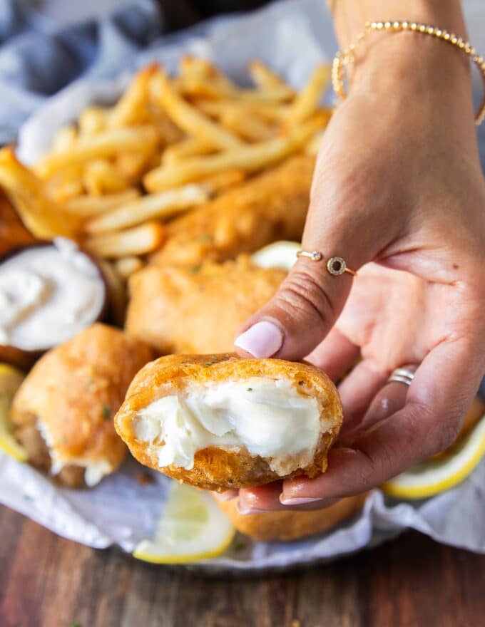 A hand holding a bitten fish showing close up the crispy crust and the succulent fish inside