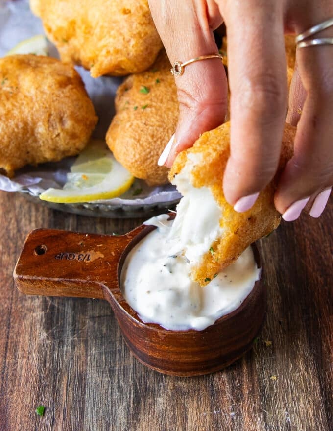 A hand dipping the fish into tartar sauce