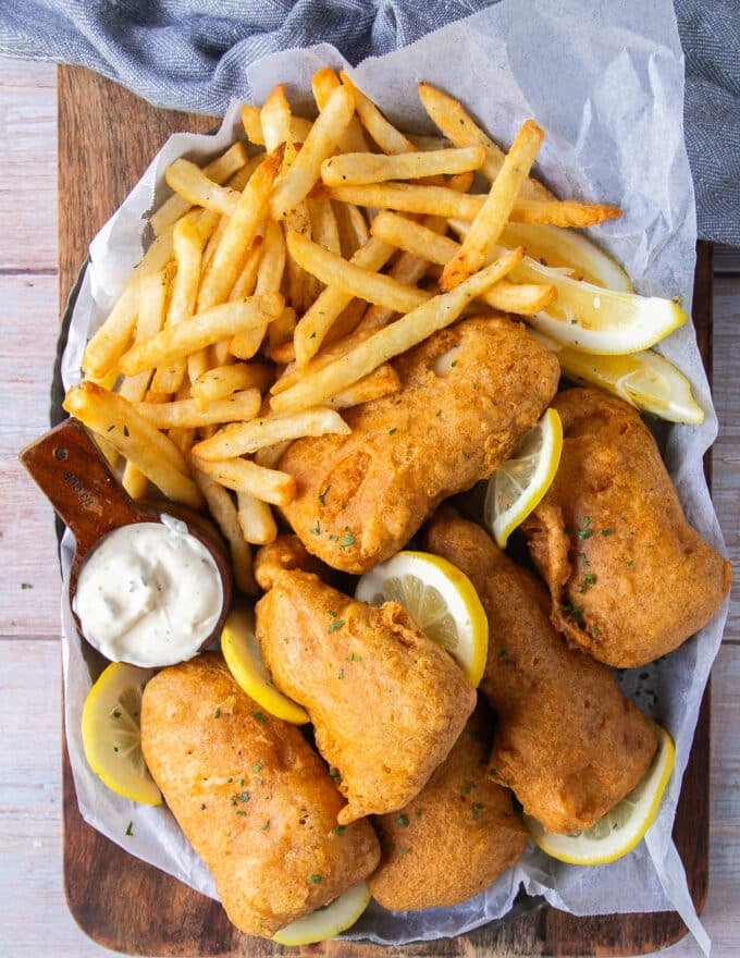 A plate full of fish and chips fried and crispy with lemon wedges and tartar sauce