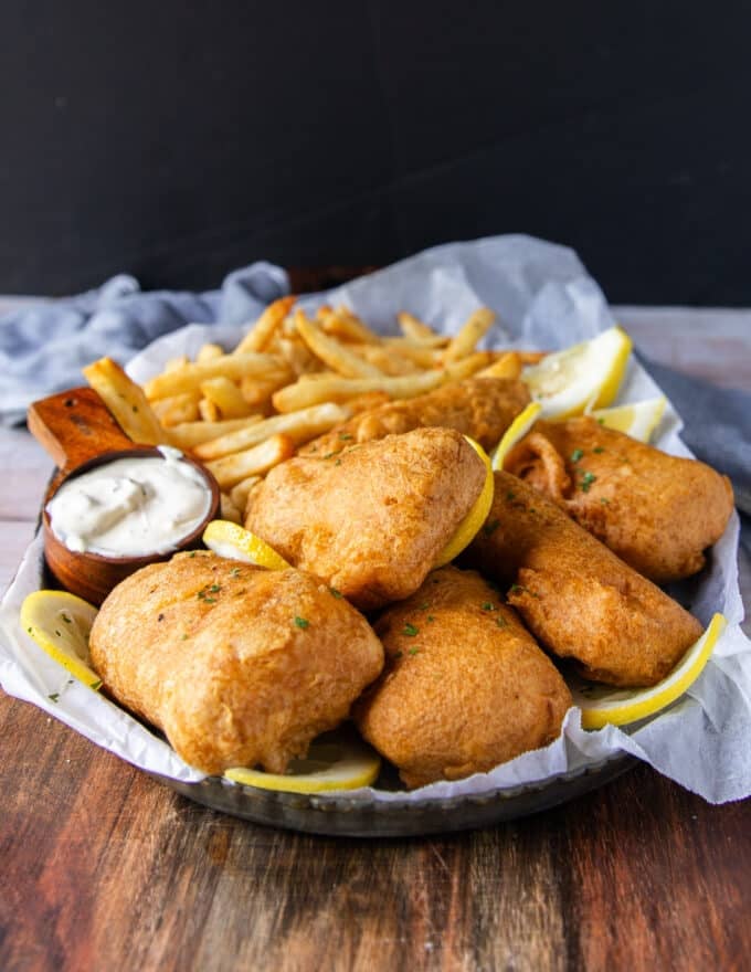 A plate of fish and chips with lemon wedges and tartare sauce