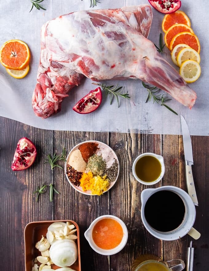 A spread of all ingredients needed to roast a lamb shoulder including spices in small bowls, balsamic vinegar , fresh herbs and olive oil