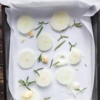 Onion slices, whole garlic cloves and fresh herbs layer the bottom of the roasting pan
