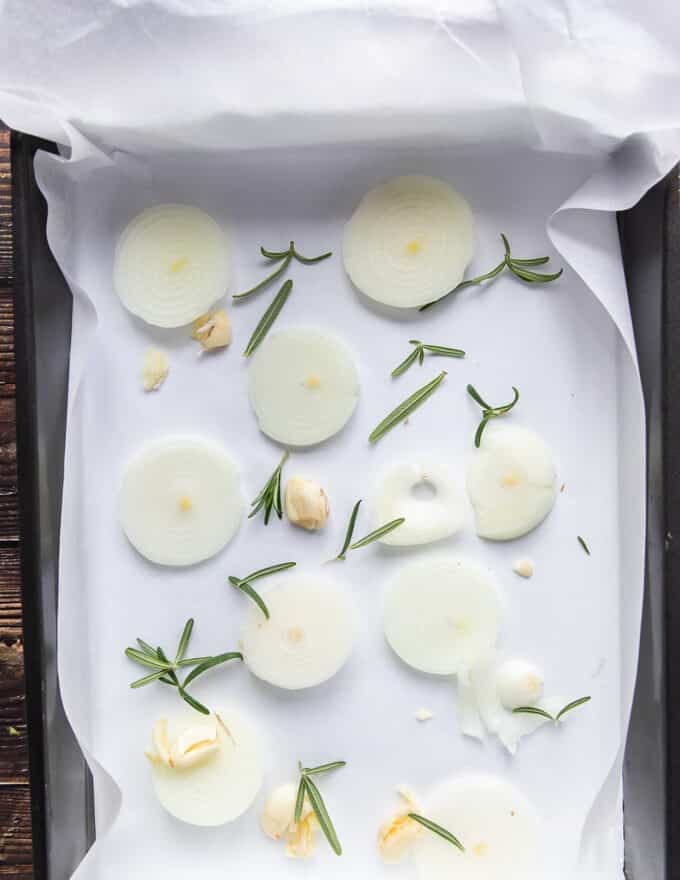 Onion slices, whole garlic cloves and fresh herbs layer the bottom of the roasting pan