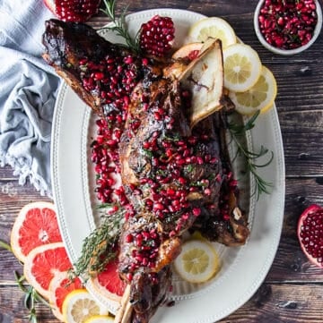 a whole lamb shoulder roasted on a plate with pomegranate arils and rosemary and orange