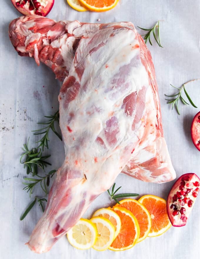 A wole lamb shoulder on parchment paper with some orange slices around it 