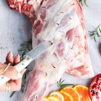 A sharp knife making incisions along the lamb shoulder