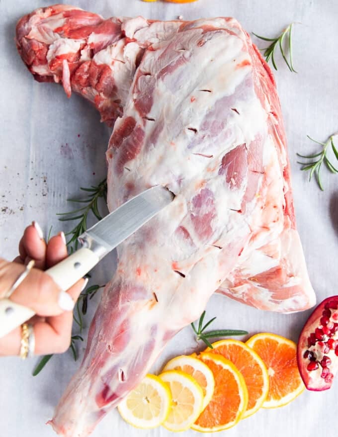A sharp knife making incisions along the lamb shoulder 