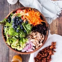 Ingredients to make apple salad including a bowl wit all the salad ingredients, some maple pecans ingredients and a maple vinaigrette