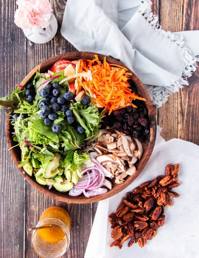 Ingredients to make apple salad including a bowl wit all the salad ingredients, some maple pecans ingredients and a maple vinaigrette