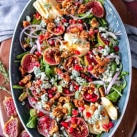 salad ingredients are piled together including arugula fresh figs, nuts, blue cheese, red onions, apples and avoocado