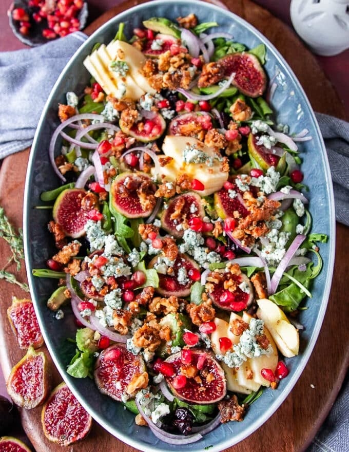 salad ingredients are piled together including arugula fresh figs, nuts, blue cheese, red onions, apples and avoocado