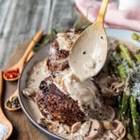 A hand spooning generous amount of mushroom sauce over the steak