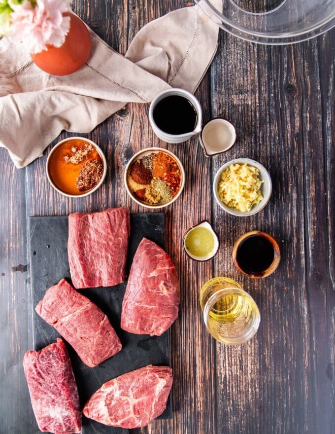 Ingredients to make flank steak tacos including the flank steak, the marinade ingredients in small bowls, the remaining taco toppings in small bowls separate on a board