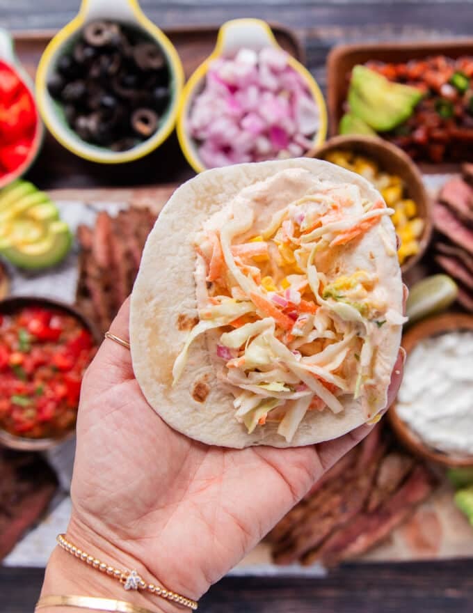 assembling the flank steak tacos starting with a tortilla and some taco slaw.