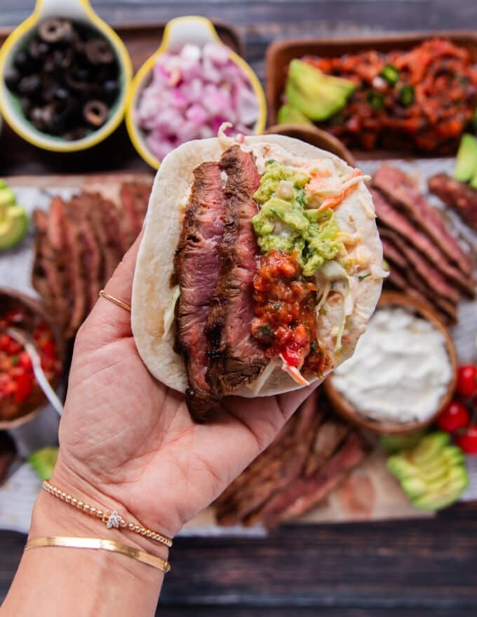continuing to assemble the flank steak tacos with the steak added, some guacamole, some salsa, and corn salad