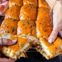 Cheese burger sliders our of the oven and hands stretching them apart showing the cheesy melt