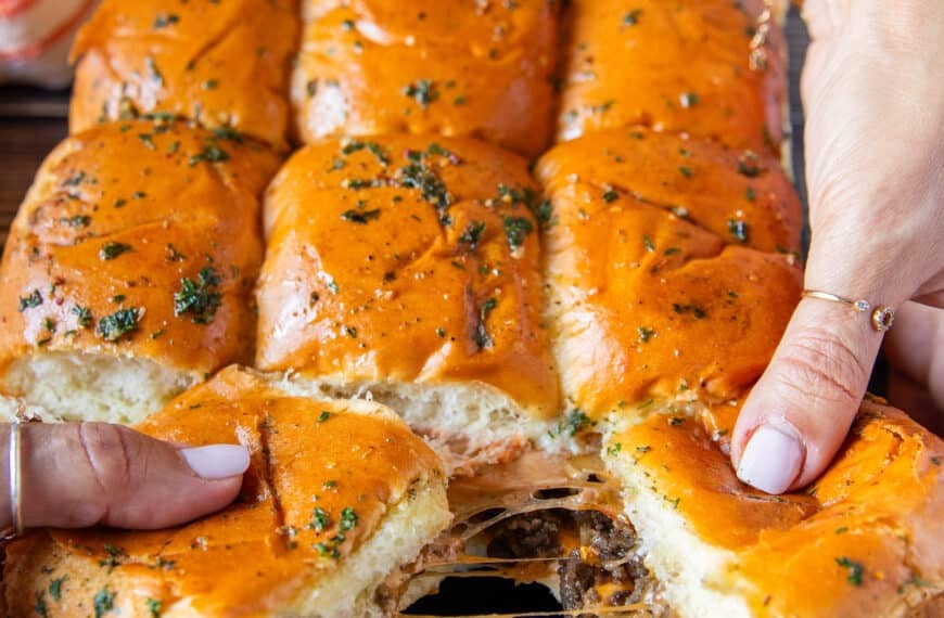 Cheese burger sliders our of the oven and hands stretching them apart showing the cheesy melt