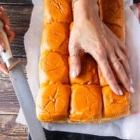 A hand using a serrated knife to cut the slider bread in half