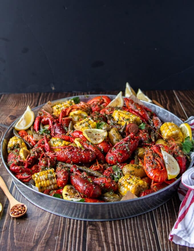 close up of a crawfish boil with crawfish , corn, potatoes, sausage, green beans and lemon wedges on a large platter ined with newspaper