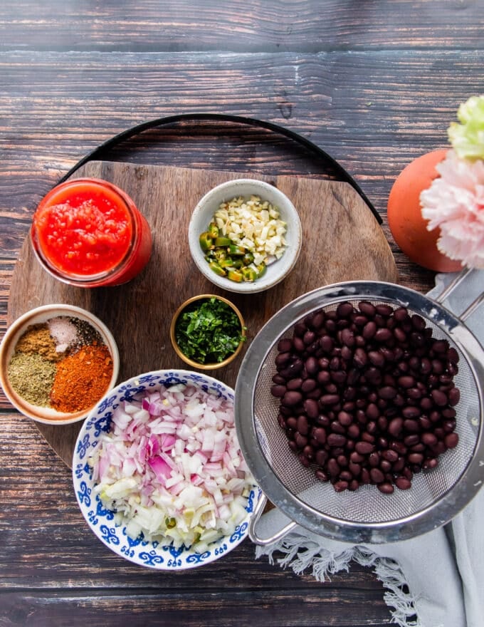 All ingredients needed to make Mexican black beans in small bowls on a wooden board 